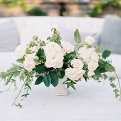 a white vase filled with lots of flowers on top of a table covered in greenery