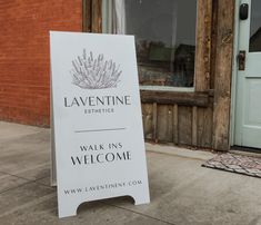 a white sign sitting on the side of a sidewalk next to a door and window