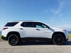 a white suv is parked on the side of the road near some grass and water