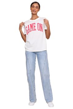 Get ready to level up your wardrobe with the Game On Boyfriend Tee! This stylish white tee featuring bold red writing and a fun "Game On" graphic will have you looking and feeling confident. Whether you're hitting the gym, running errands, or just lounging around, this tee is the perfect blend of comfort and style. Model is 5'10" wearing a size XS 100% Cotton Machine wash cold Hang or line dry Casual White T-shirt With Logo Lettering, Casual Tops With Logo Lettering, Trendy White T-shirt With Lettering, White Hip Hop Slogan Top, Trendy Sports T-shirt, Cotton Team Spirit T-shirt With Slogan, White Sporty Tops With Logo Lettering, Sporty White Tops With Logo Lettering, White Athleisure T-shirt For College