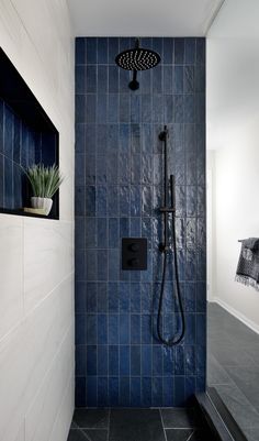 a blue tiled shower in a bathroom with black tile flooring and wall mounted shower head