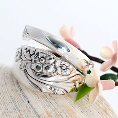 two silver rings sitting on top of each other with flowers in the middle and leaves around them