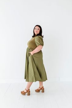 Features Mock neck Short puff sleeves with elastic Ribbed bodice Elastic waist Olive color Pockets 60% Cotton, 40% Polyester; Contrast: 52% Viscose, 26% Polyester, 22% Nylon Size + Fit Small 0-4, Medium 4-8, Large 8-12, X-Large 14-16, 1X 16-18, 2X 20-22, 3X 24-26 Kristin is 5'4", a size 1 and is wearing a Small Jaycie is 5'6" a size 18 and is wearing a 2X Runs true to size. Measurements taken while laying flat and then doubled. They do no account for stretch. Size Bra Band Length Small 34" 46" M Spring Dresses With Elastic Shoulders And Stretch, Spring Dresses With Stretch Elastic Shoulders, Fitted Midi Dress With Elastic Waistband For Daywear, Fitted Solid Color Dress With Elastic Waistband, Modest Fitted Puff Sleeve Dress With Short Sleeves, Green Puff Sleeve Dress With Gathered Balloon Sleeves, Fitted Midi Dress With Puff Sleeves And Gathered Waist, Fitted Midi Dress With Gathered Waist And Puff Sleeves, Modest Fitted Puff Sleeve Dress