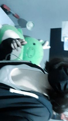 a person laying down with a green teddy bear on their lap and other items in the background