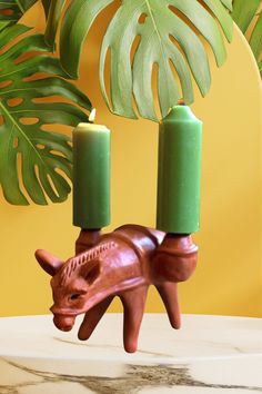 two candles in the shape of a rhinoceros head on a table next to a plant