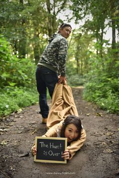 two people in the woods with a sign that says the hunt is over and there is a woman laying on the ground