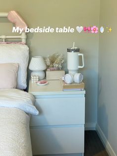 a white bed sitting next to a night stand with a cup on top of it