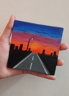 a hand holding up a small painting of a sunset