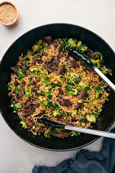 a wok filled with noodles and broccoli on top of a white table