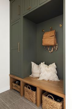 a wooden bench with two baskets and a purse hanging on the wall above it, in front of green cupboards