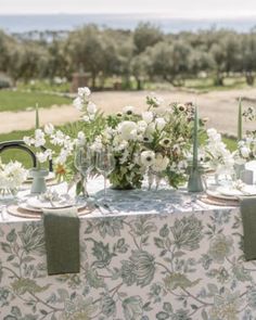 the table is set with white flowers and greenery for an outdoor dinner party or reception