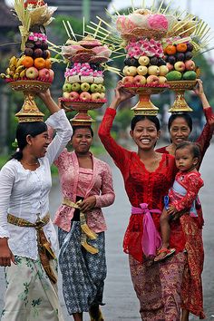 a group of women carrying trays with fruit on them