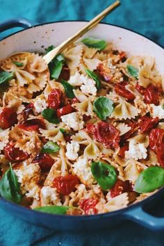 a pasta dish with tomatoes, spinach and feta cheese in a blue pan