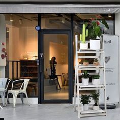 a store front with plants and chairs outside