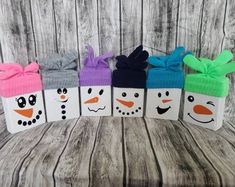 four snowman gift boxes with bows and faces painted on the sides, sitting in front of a wooden background