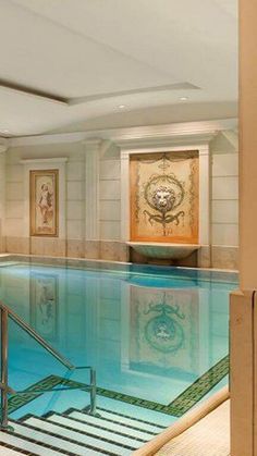 an indoor swimming pool with stairs leading up to the water and paintings on the wall