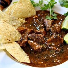 a bowl of beef chili with tortilla chips and cilantro on the side