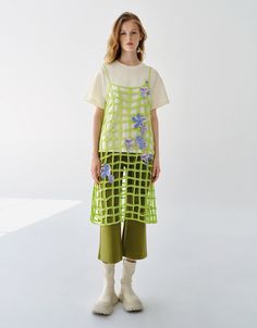 a woman standing in front of a white background wearing green pants and a t - shirt with flowers on it