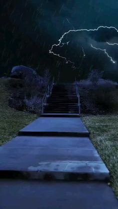 a path leading up to a set of stairs with lightning in the background