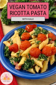 a blue plate topped with pasta covered in tomatoes and spinach next to lemon wedges