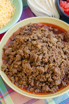 a bowl filled with meat and vegetables on top of a checkered table cloth next to bowls of food