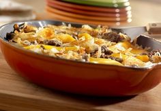 a casserole dish with cheese and meat in it on a wooden table next to a green plate