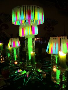 a table topped with lots of lit up candles next to green and yellow lights on top of glass vases