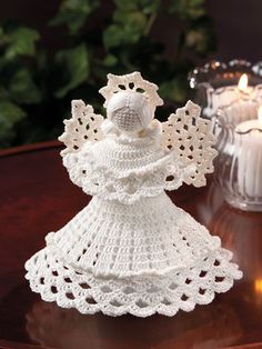 a crocheted angel sitting on top of a table next to a lit candle