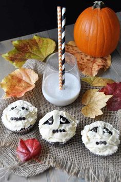 halloween cupcakes with frosting and candy on a table next to pumpkins