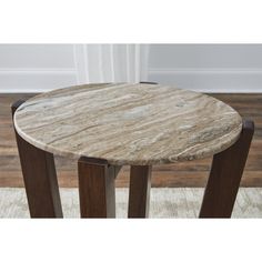 a round marble table with wooden legs on a rug in front of a white wall