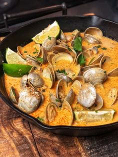 a skillet filled with clams and sauce on top of a wooden table