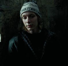 a young man wearing a beanie standing in front of a stone wall