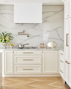 a kitchen with white cabinets and marble counter tops, gold pulls on the faucet