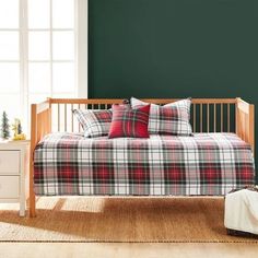 a day bed with plaid sheets and pillows in a green room next to a christmas tree