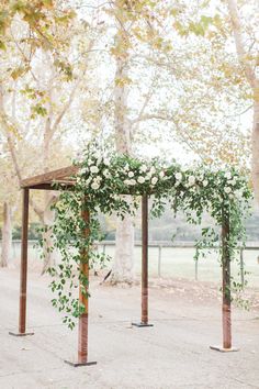 an outdoor ceremony setup with flowers and greenery on the arbors, surrounded by trees