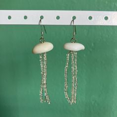 two white beads hanging from hooks on a green wall next to a pair of earrings