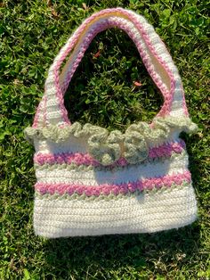 a crocheted purse sitting on top of green grass covered in pink and white yarn