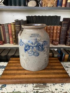 a white vase sitting on top of a wooden board in front of bookshelves