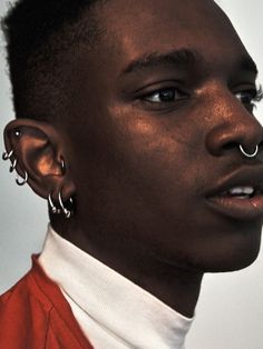 a man with piercings on his nose wearing a red jacket and white turtle neck shirt