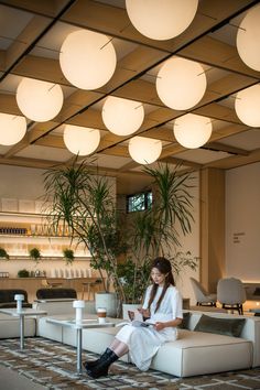 a woman is sitting on a couch in an office lobby with lights hanging from the ceiling