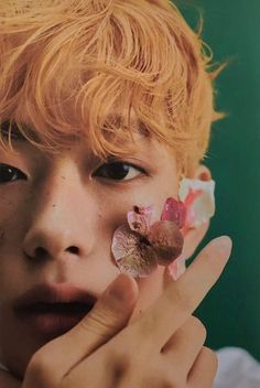 a person with flowers in their hair holding something up to her face and looking at the camera