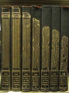 a row of black books sitting on top of a wooden book shelf next to each other