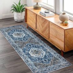 a large blue rug on top of a wooden floor next to a dresser and potted plant