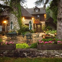 an outdoor patio with tables and chairs next to a stone house at night in the evening