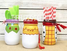 three decorated mason jars sitting next to each other on top of a wooden table with paper straws in them