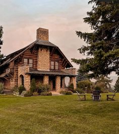 an old log cabin sits in the middle of a grassy field with two lawn chairs