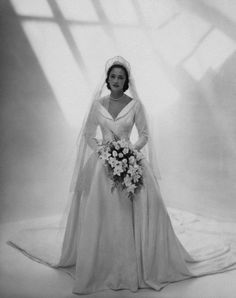 an old photo of a woman in a wedding dress and veil holding a flower bouquet