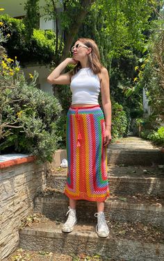 a woman standing on the steps wearing a colorful skirt and white tank top with her hands in her pockets