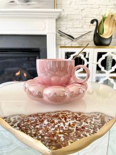 a pink coffee cup sitting on top of a white table next to a fire place