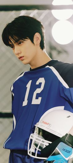 a young man wearing a football uniform and holding a helmet in one hand, looking to the side